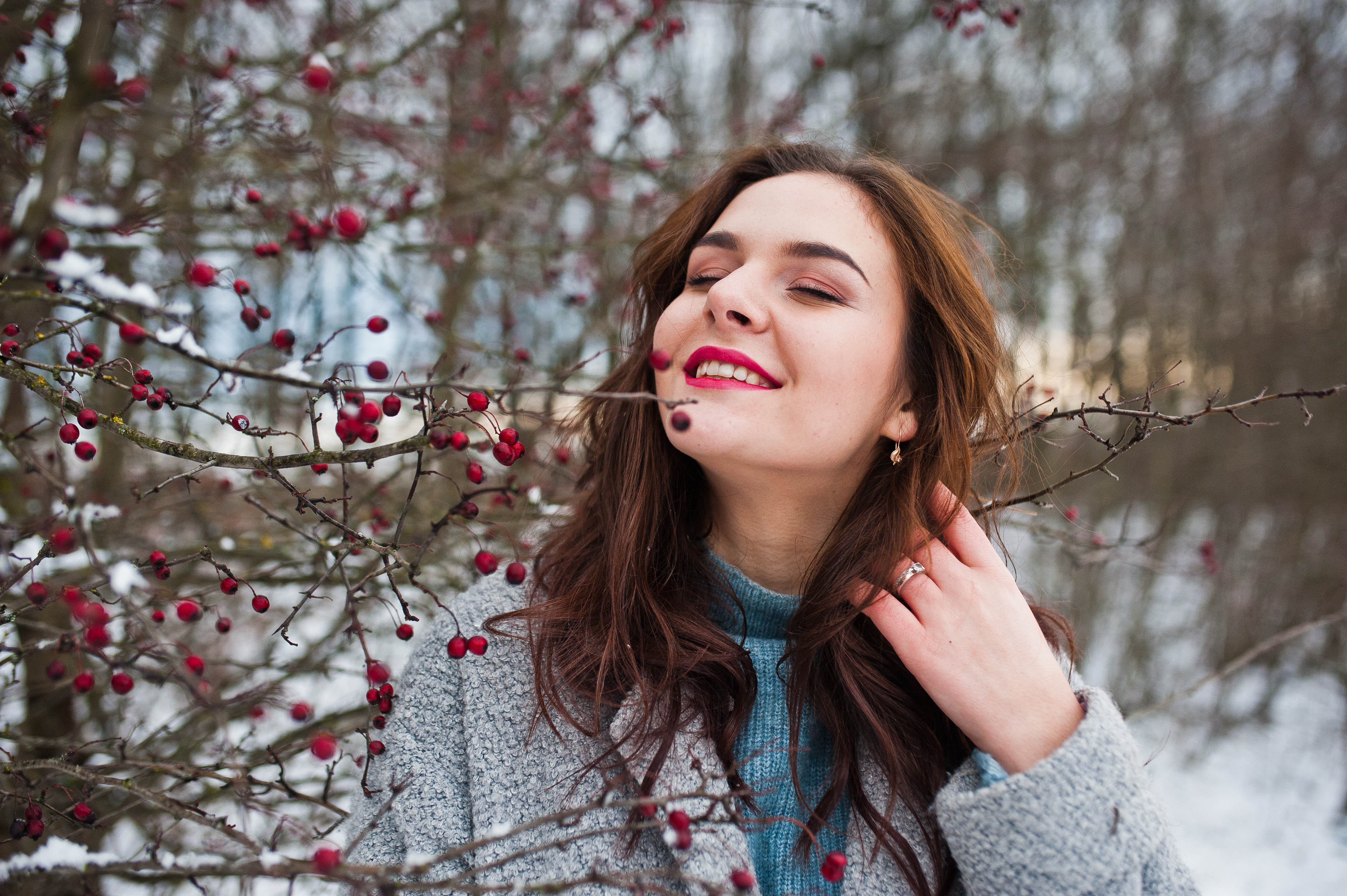 Close up portrait of gentle girl in gray coat near the branches of a snow-covered tree.