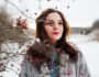 Close up portrait of gentle girl in gray coat near the branches of a snow-covered tree.